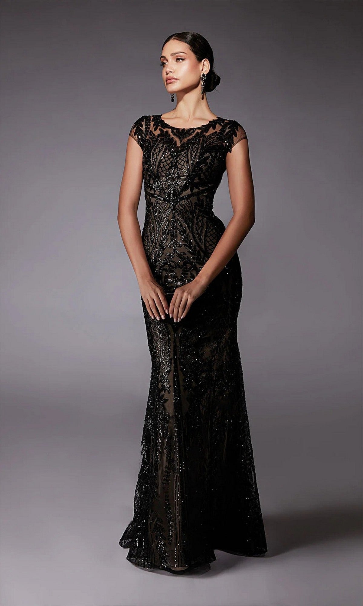 A woman models the Alyce 27716, a long, fitted black formal dress featuring intricate beading and short sleeves—an elegant mother-of-the-bride choice—set against a plain gray background.